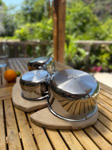 Casseroles en inox Pranacook posées sur une planche en bois, extérieur ensoleillé