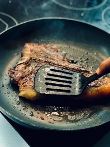 a hand frying a meat on black pan