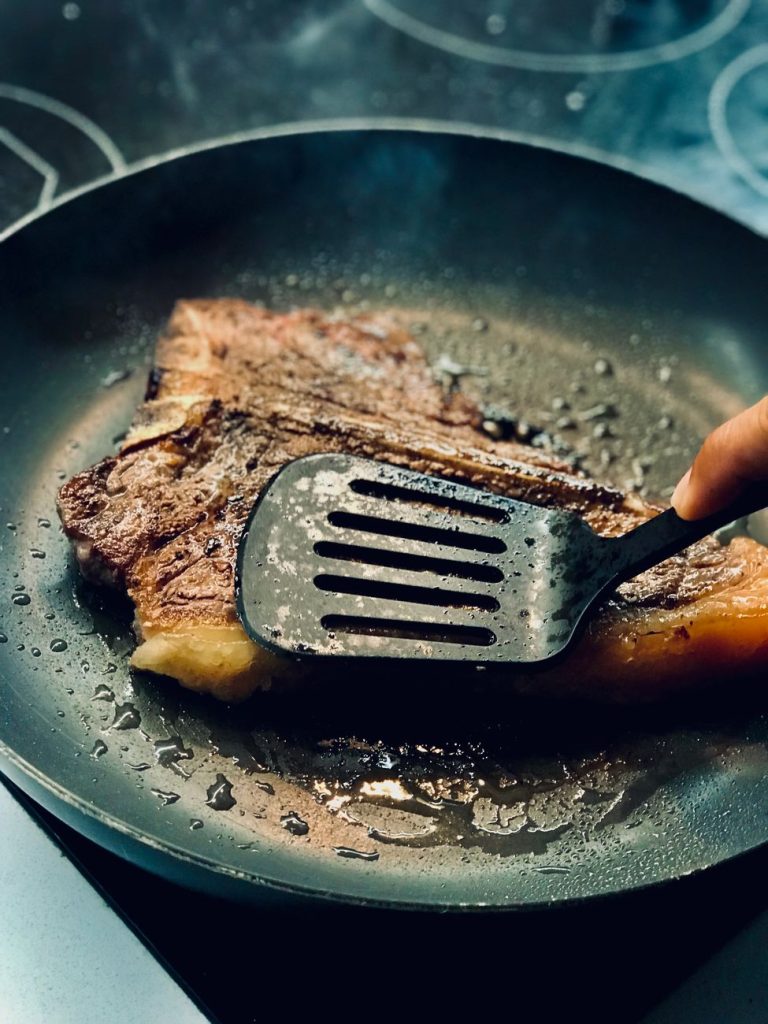 a hand frying a meat on black pan